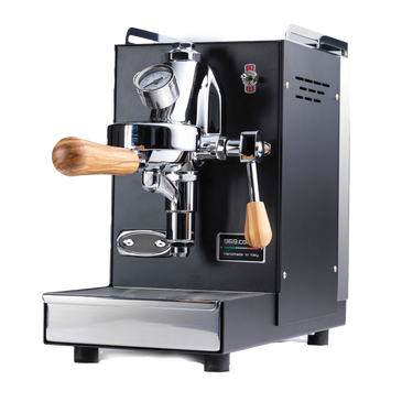 Die Espressomaschine Elba Mini in schwarz mit Olivenholzgriff. In der Mitte befindet sich die Faema E-61 Brühgruppe. Darunter die herausziehbare Abtropftasse. Darüber eine Reling um das Herunterfallen der Tassen zu vermeiden, dahinter der abnehmbare Edelstahl Wassertank.