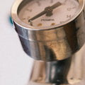 Eine Detailaufnahme des verchromten Brühdruckmanometers auf einer E-61 Brühgruppe. Zu sehen ist das weiße Ziffernblatt mit einer Skalierung  bis 16bar, darunter die Aufschrift „Pompa“