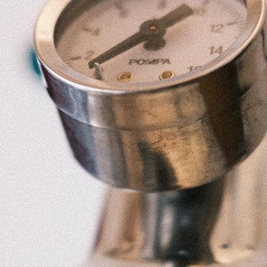 Eine Detailaufnahme des verchromten Brühdruckmanometers auf einer E-61 Brühgruppe. Zu sehen ist das weiße Ziffernblatt mit einer Skalierung  bis 16bar, darunter die Aufschrift „Pompa“