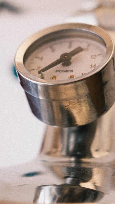 Eine Detailaufnahme des verchromten Brühdruckmanometers auf einer E-61 Brühgruppe. Zu sehen ist das weiße Ziffernblatt mit einer Skalierung  bis 16bar, darunter die Aufschrift „Pompa“