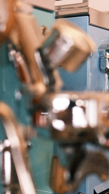 Zu sehen ist im Vordergrund verschwommen ein Teil der Brühgruppe der Espressomaschinen Elba Quattro in türkis, dahinter scharf ein kleiner Teil derselben Maschine in hellblau.