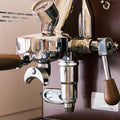Zu sehen ist die Espressomaschine Elba Mini in Bordeaux-Rot mit Sieträgergriff und Kipphebelknauf aus Walnuss Holz. In der Mitte der Brühgruppe befindet sich ein Brühdruck Manometer, auf der linken Seite die einstellbare PID Temperaturkontolle. Darunter die herausziehbare Abtropftasse. Darüber eine Reling um das Herunterfallen der Tassen zu vermeiden.