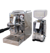 Zu sehen ist die Espressomaschine Quickmill Carola Evo in Edelstahl. In der Brühgruppe ist ein Siebträger mit schwarzem Kunststoffgriff für 2 Tassen eingespannt auf der rechten Seite die einstellbare PID Temperaturkontrolle. Rechts oben befindet sich das Brühdruck-Manometer. Darunter die herausziehbare Abtropftasse. Darüber eine Reling um das Herunterfallen der Tassen zu vermeiden. Daneben ist die On-Demand Kaffeemühle Eureka Mignon Silenzio in chrom abgebildet.