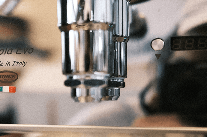 Eine Detailaufnahme der Espressomaschine Quickmill Carola. Links ist der Schriftzug Carola Evo Made in Italy zu sehen. Mitte der untere Teil der Faema E-61 Brühgruppe. Auf der rechten Seite sieht man die verstellbare PID Steuerung.