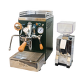 Zu sehen ist die Espressomaschine Elba Quattro in British Racing Green mit Siebträgergriff, Kipphebelknauf und Drehrad für Dampf aus Olivenholz. In der Mitte der Brühgruppe befindet sich ein Brühdruck Manometer, auf der rechten Seite das Kesseldruck-Manometer. Darunter die abnehmbare Abtropftasse. Darüber eine Reling um das Herunterfallen der Tassen zu vermeiden. Daneben ist die On-Demand Kaffeemühle Eureka Mignon Silenzio in chrom abgebildet.