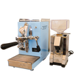 Zu sehen ist die Espressomaschine Elba Mini in hellblau mit Sieträgergriff und Kipphebelknauf aus schwarzem Holz. In der Mitte der Brühgruppe befindet sich ein Brühdruck Manometer, auf der linken Seite die einstellbare PID Temperaturkontolle. Darunter die herausziehbare Abtropftasse. Darüber eine Reling um das Herunterfallen der Tassen zu vermeiden. Daneben ist die On-Demand Kaffeemühle Eureka Mignon Silenzio in chrom abgebildet.