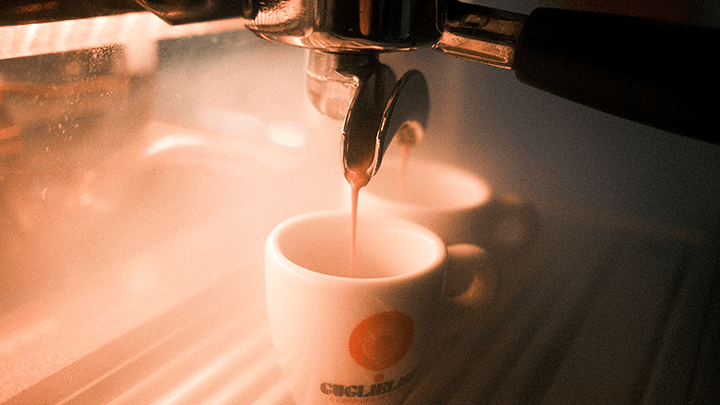 Kaffeezubereitung mit der 3-gruppigen Handhebel Kaffeemaschine SM Leva Luxury. In diesem Detail sieht man Kaffee in 2 weiße Guglielmo Tassen rinnen. Im Hintergrund etwas verschwommen die durch Dampf beschlagene Glasverkleidung.