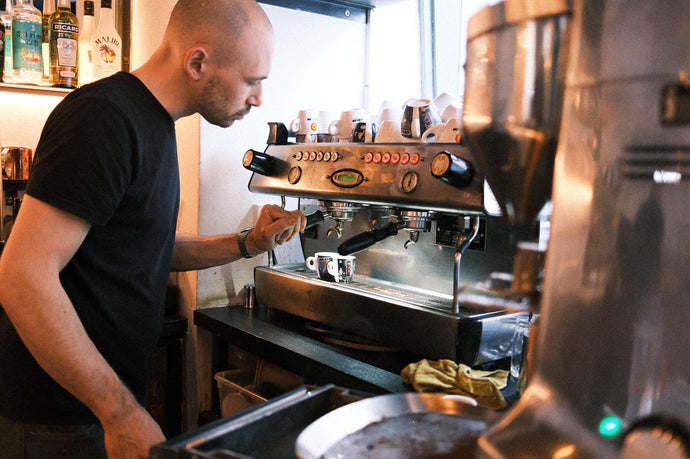 Zu sehen ist der Firmenchef beim Einstellen des Mahlgrades bei einem Gastrokunden.
Es wird dabei bei einer La Marzocco GB5 ein doppelter Espresso zubereitet.