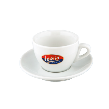 Eine weiße dickwandige Cappuccinotasse mit Unterteller mit dem Henkel auf der rechten Seite. In der Mitte der Tasse ist der weiße Ionia Schriftzug auf rot/blauem Hintergrund abgebildet.