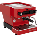 Die Schrägansicht von vorne der Espressomaschine La Marzocco Linea Mini R in rot. An der Oberseite ist das Paddle für den Kaffeebezug angebracht, links davon das Drehrad für Teewasser, rechts davon das Drehrad für die Dampflanze. Darunter befindet sich die Brühgruppe mit dem eingespannten Siebträger mit schwarzem Griff, darunter die Abtropftasse.