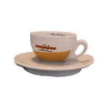 Eine weiße dickwandige Cappuccinotasse mit Unterteller mit dem Henkel auf der rechten Seite. In der Mitte der Tasse ist der rote Kremoso Schriftzug abgebildet, das untere Drittel der Tasse ist gelb.
